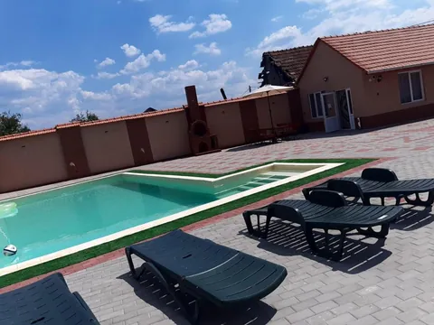 Șezlonguri lângă piscină, cu acoperișurile de țiglă ale pensiunii